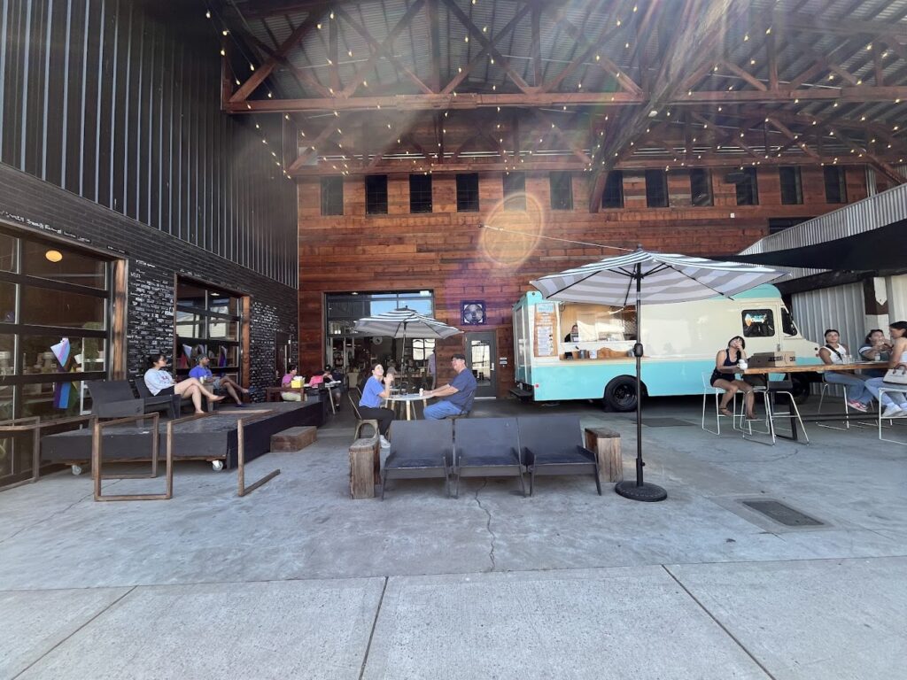 One of the outdoor spaces at Mac Market. It's covered and has a variety of places to sit. There's a blue food truck outside.