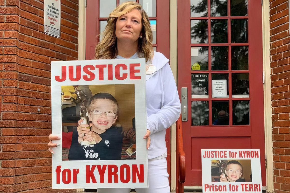 Desiree Young, Kyron Horman's mother, stands on the steps of Skyline Elementary School. She holds a large sign with Kyron's photo that reads "JUSTICE FOR KYRON".
