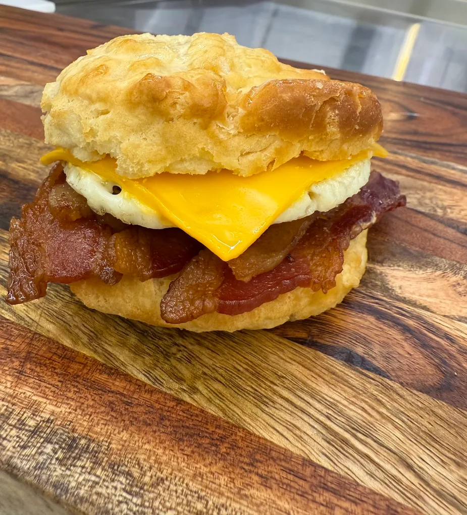 A breakfast sandwich made of thick bacon, eggs and a slice of cheese in between two slices of a breakfast biscuit. It looks really good.