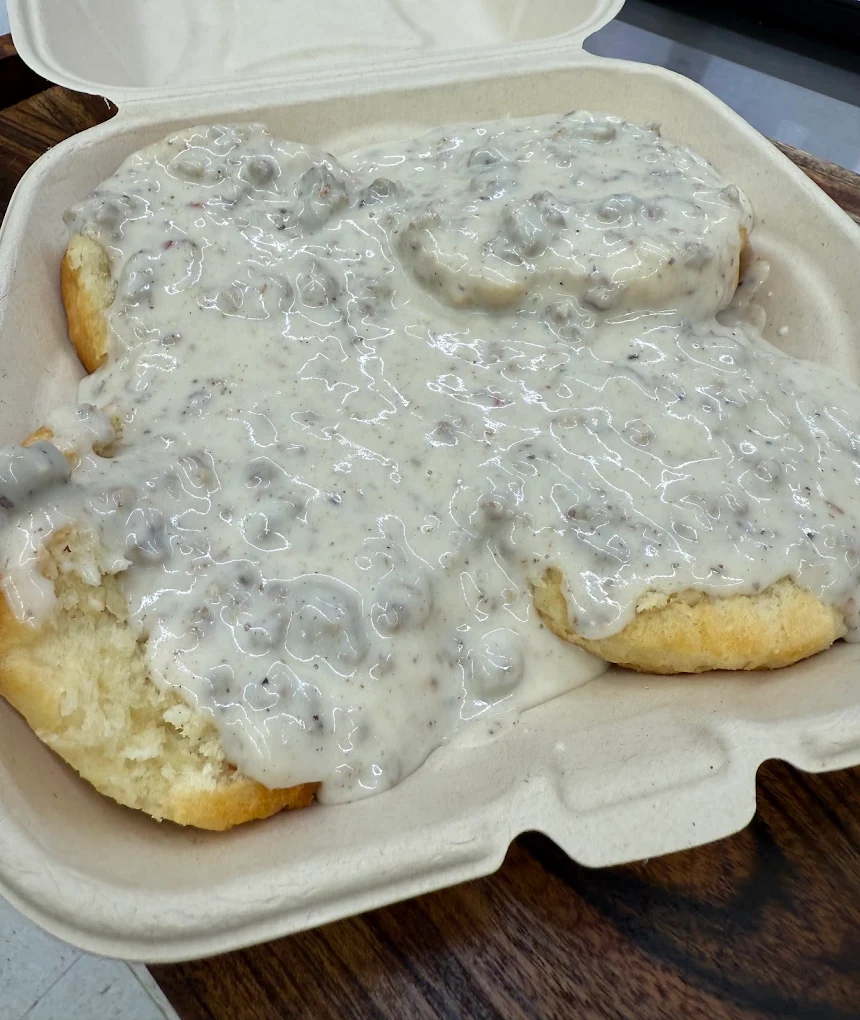 A white takeout container filled with biscuits and country gravy. It looks delicious!