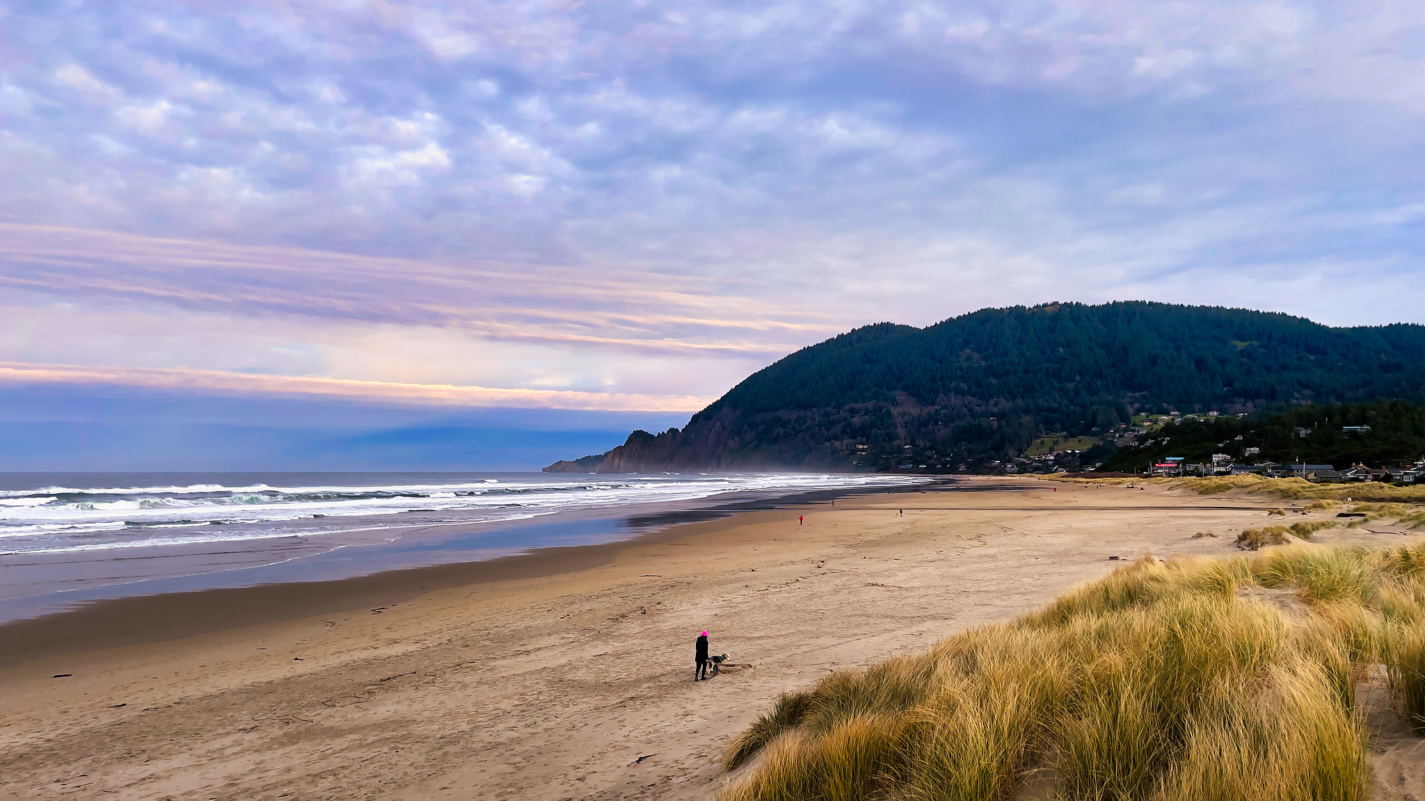 A woman walks a dog down a sandy beach in Manzanita, Oregon.