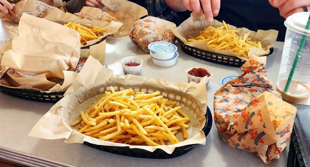 Fries and burgers in black basket containers sitting on a table at Burgerville.