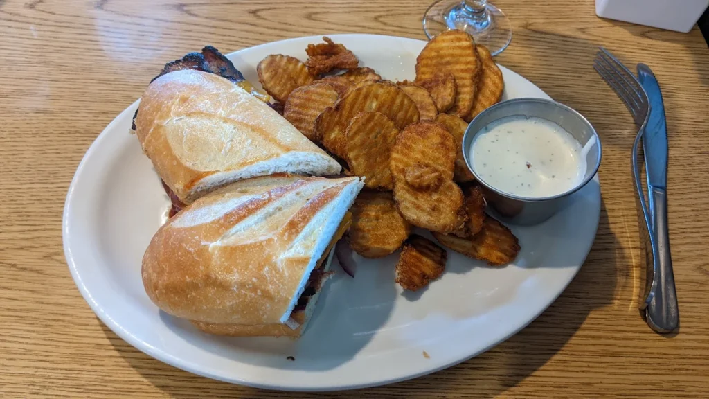 A meat sandwich with pickle chips and dip on a white plate.