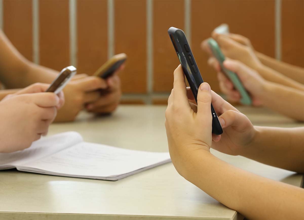 Students sit at a desk looking at their cell phones.
