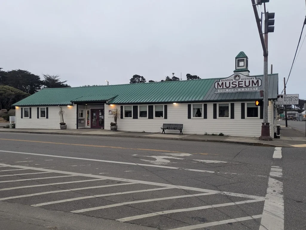 The outside of the Bandon Historical Society Museum. It's a white building, with red shutters and a green roof.