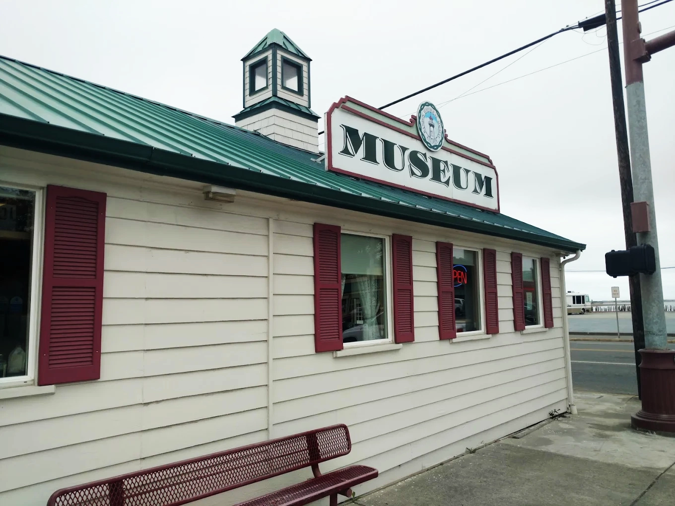 The outside of the Bandon Historical Society Museum. It's a white building, with red shutters and a green roof.