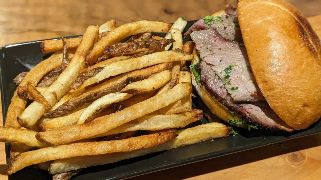 A smoked meat sandwich on a bun and hand cut fries. The fries look crispy on the outside.