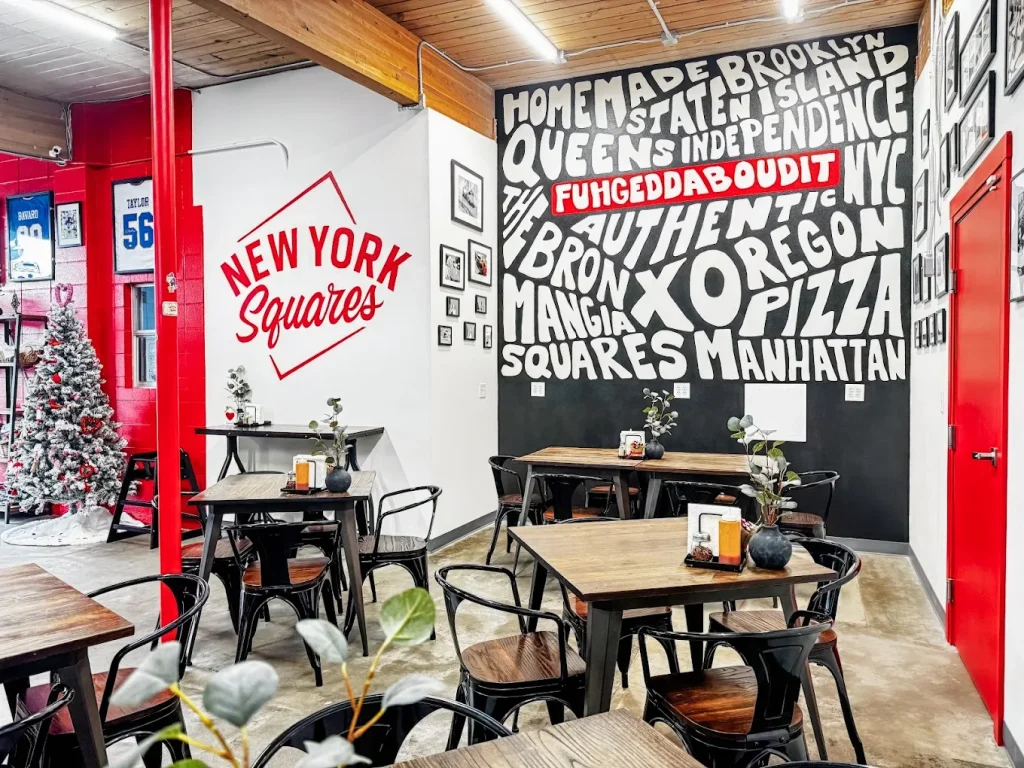 The interior of the brick and mortar New York Squares location. The wallsa re black, white, and red, with huge painted words like Oregon, Pizza, and Bronx.