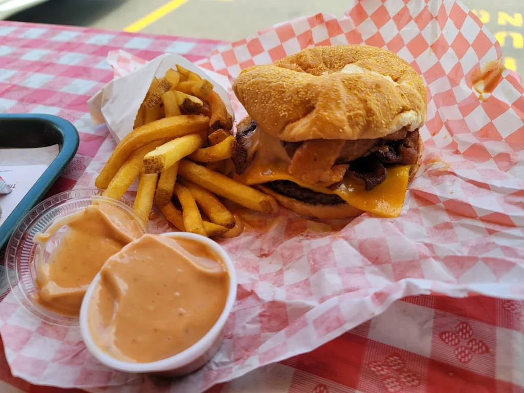 A tasty burger and fries with a container of fry sauce sitting on a red and white checkered paper.