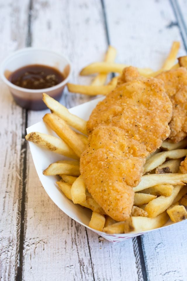 Chicken strips and fries with a container of barbecue sauce in the background.