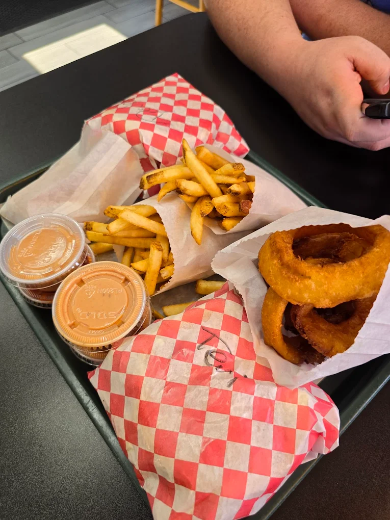 Fries, onion rings, fry sauce, and two sandwiches or burgers wrapped up in red and white checkered paper on a black tray.