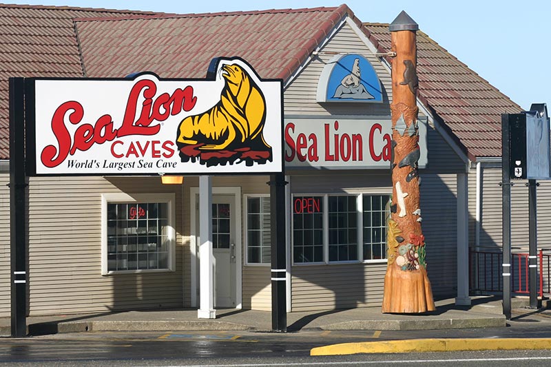 The outside of the Sea Lion Caves building. It's white with red words and a yellow drawing of a sea lion.