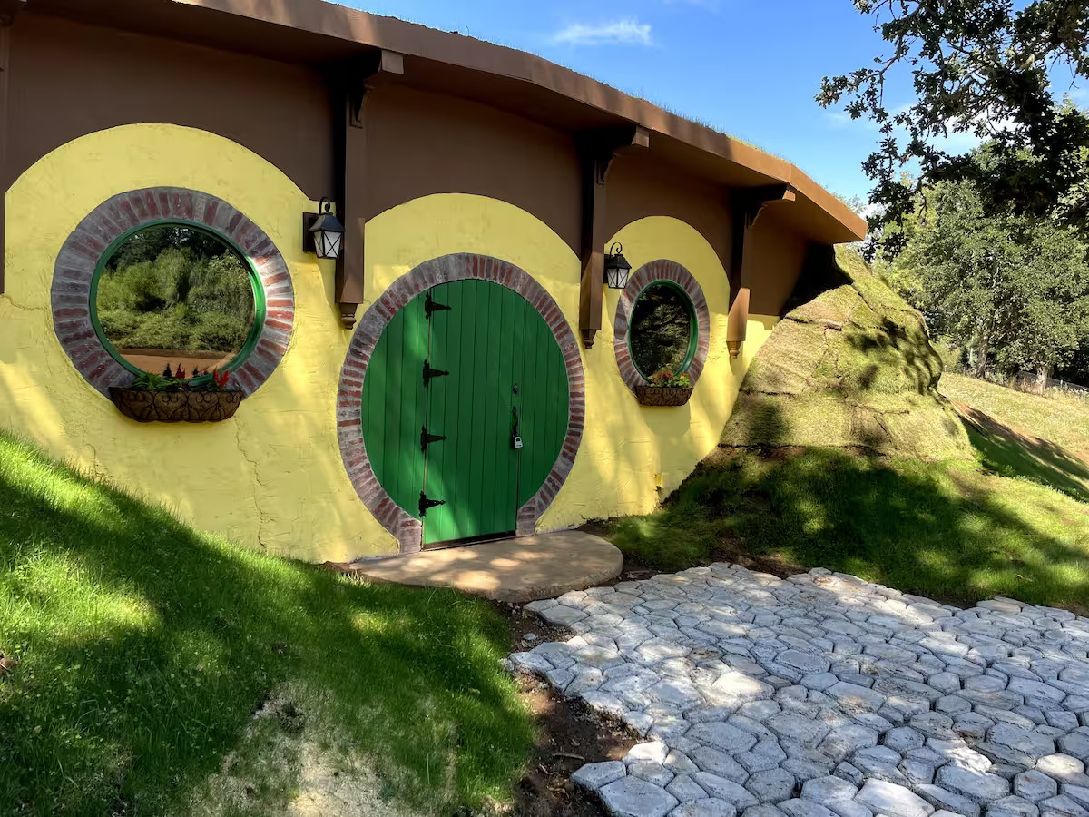 The Bag Inn sits inside a hill. Cobbles lead up to the large green front door. The front of the building is yellow and brow. It looks like a hobbit home.