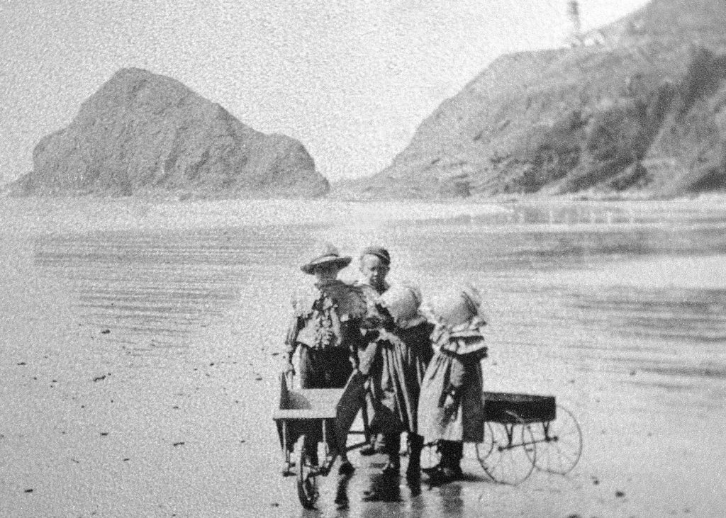 A black and white photo of children standing on the beach at Heceta Head.