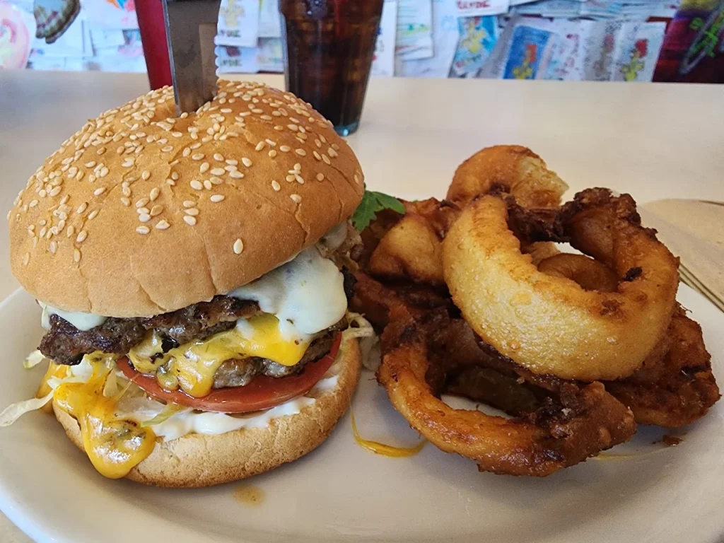 A monster looking burger with a knife sticking out the top, and huge onion rings.