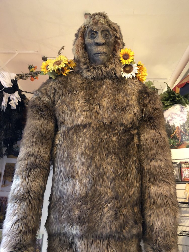 An enormous statue of bigfoot with yellow and white flowers on his shoulders.