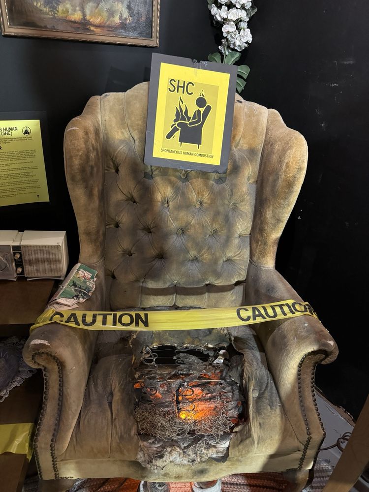 A burnt up chair with caution tape in front of it, and feet inside shoes on the floor. It looks like a person spontaneously combusted sitting there.