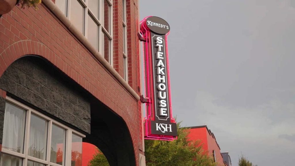 Neon Kennedy’s Steakhouse sign glowing outside the brick building on Pearl Street in downtown Eugene, Oregon.