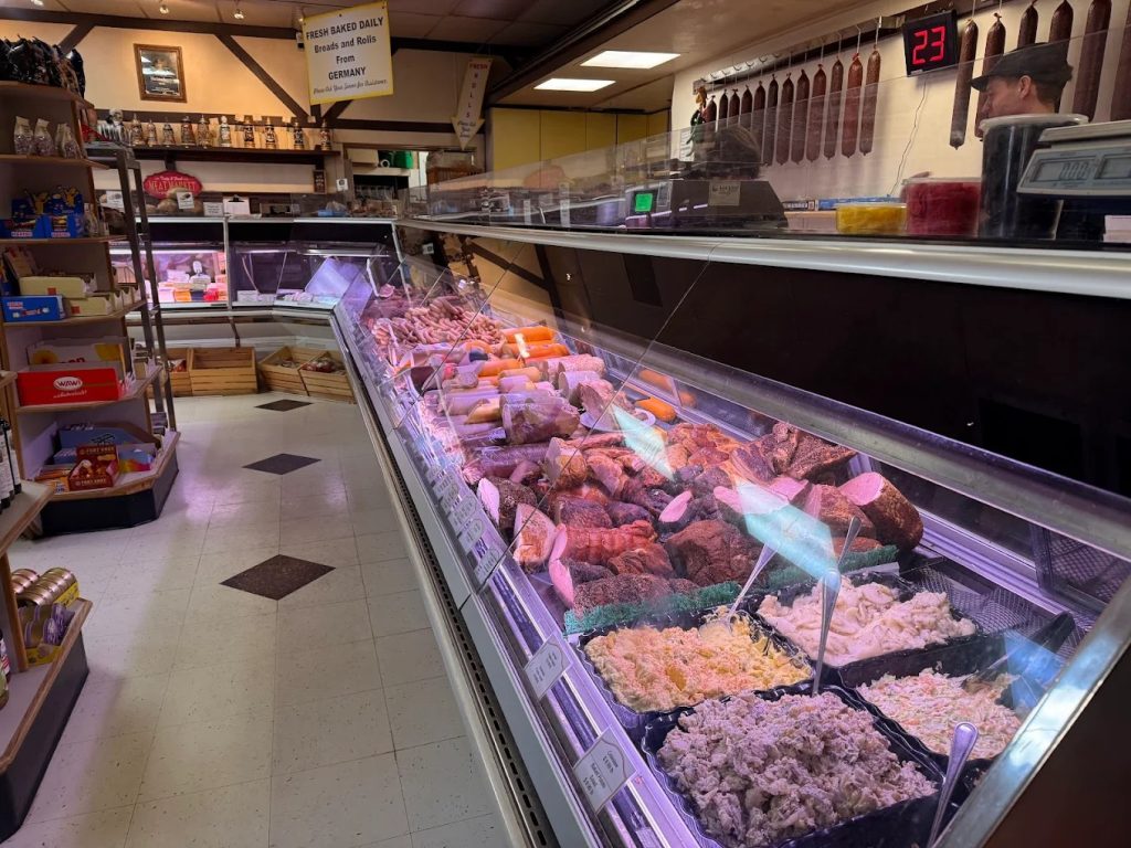 Inside a traditional German butcher shop in Portland with glass meat cases, hanging sausages, and imported foods