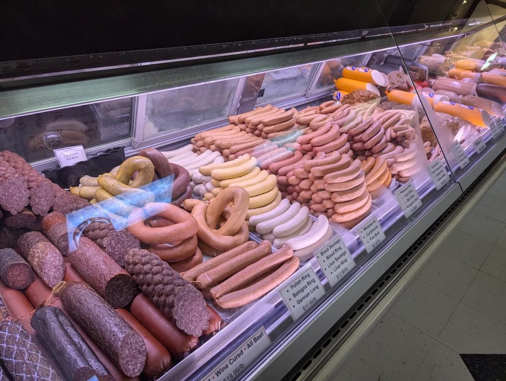 Inside a traditional German butcher shop in Portland with glass meat cases, hanging sausages, and imported foods