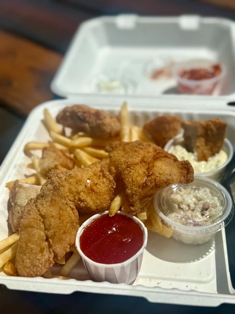 Golden fried fish and chips served at Bandon Bait in Bandon, Oregon, featuring crispy battered seafood with fries and coleslaw on a bayfront table.