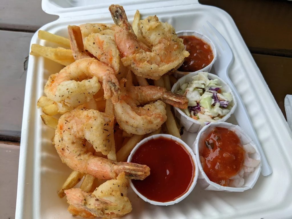 Golden fried shrimp and chips served at Bandon Bait in Bandon, Oregon, featuring crispy battered seafood with fries and coleslaw on a bayfront table.