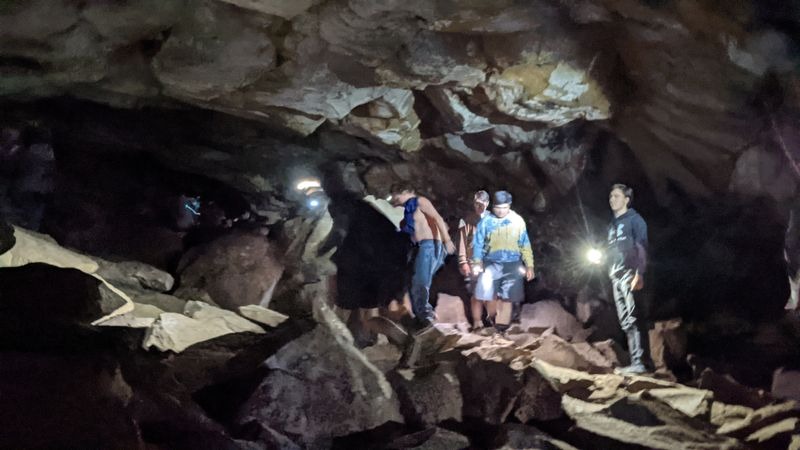 Visitors exploring uneven lava rock floor inside Lava River Cave with headlamps in Oregon