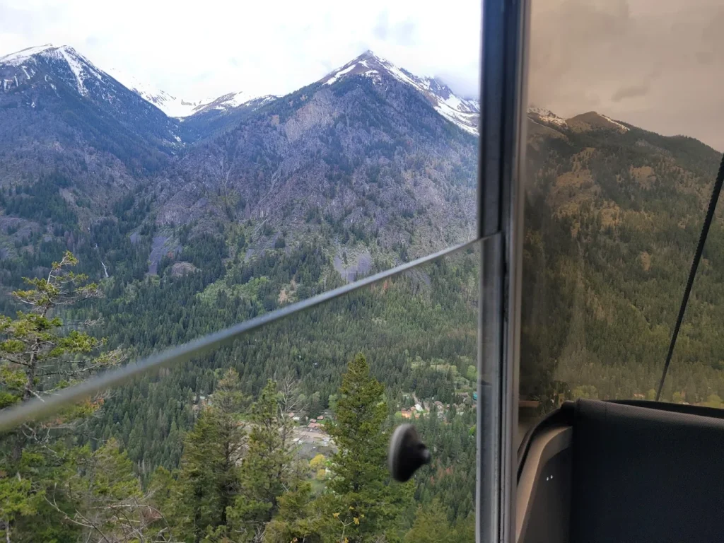 A view from inside one of the gondolas. Trees and snow capped peaks are visible close by.