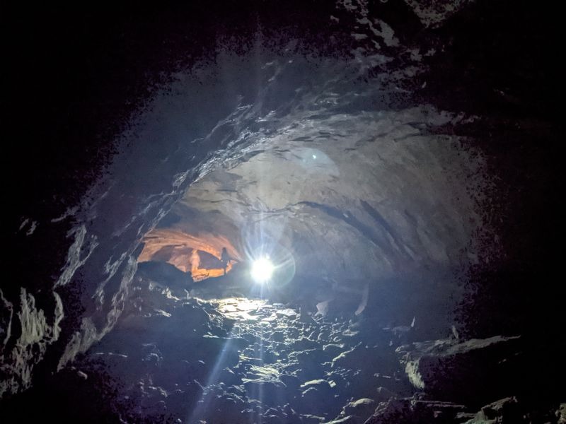 Visitors exploring uneven lava rock floor inside Lava River Cave with headlamps in Oregon