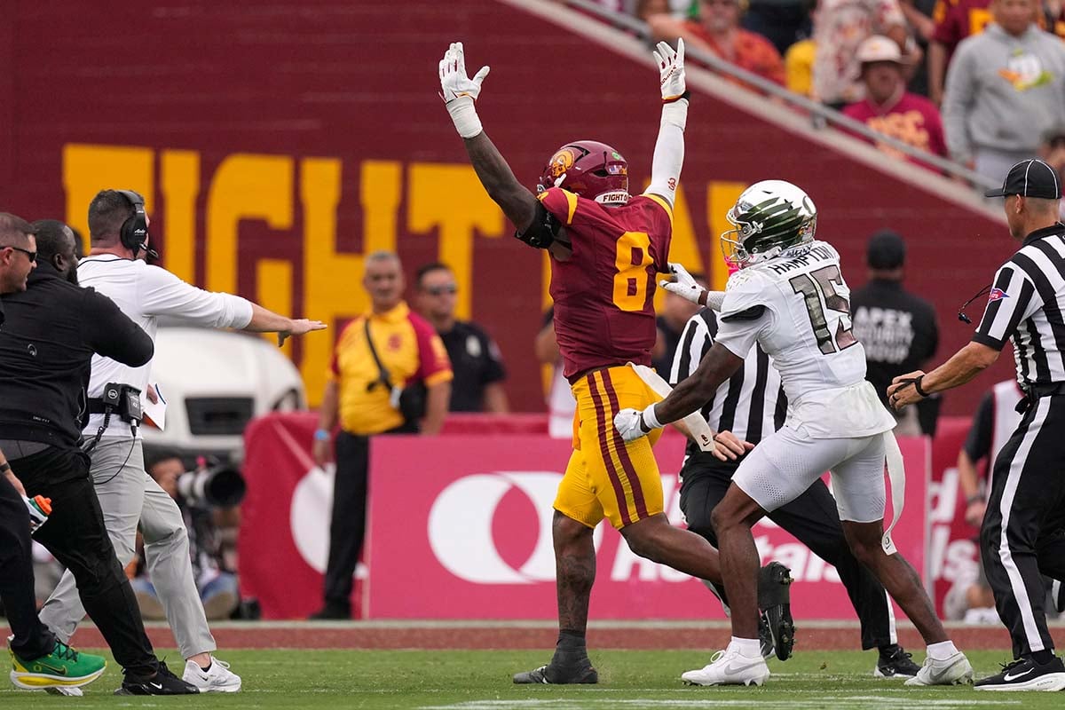 USC player No. 8 raises both arms beside Oregon player No. 15 as coaches and officials approach on the field.