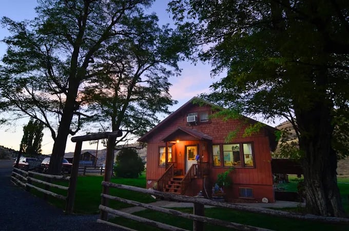 A warmly lit ranch house at dusk beneath mature trees at Wilson Ranches Retreat