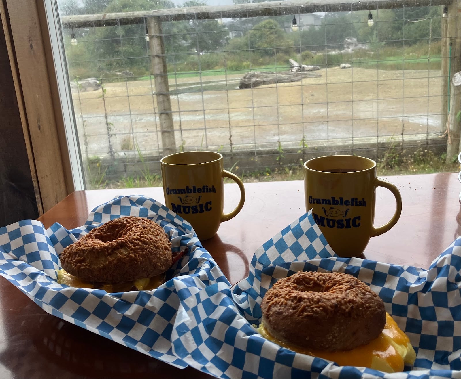 Bagel sandwiches and Grumblefish Music mugs at a window table.