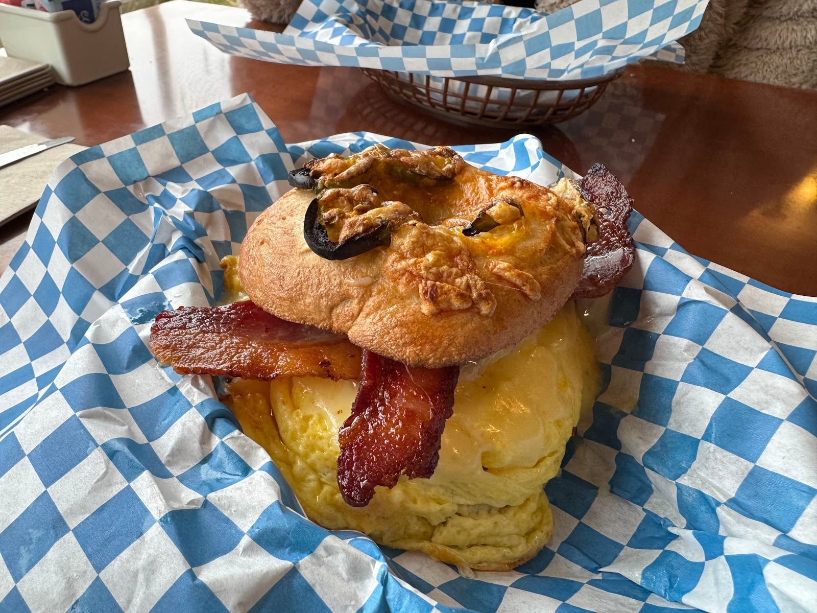 A bacon and egg sandwich on a cheese-covered bagel with jalapeño slices.