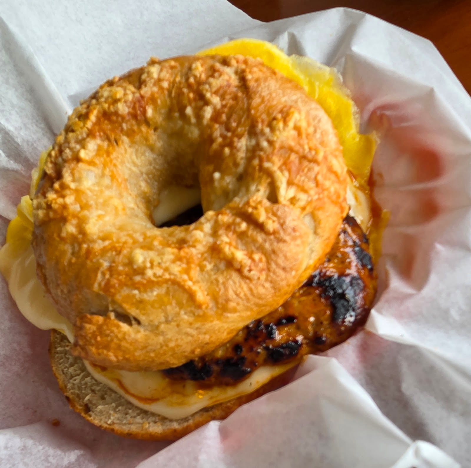 A cheese-topped bagel holds a substantial breakfast sandwich.