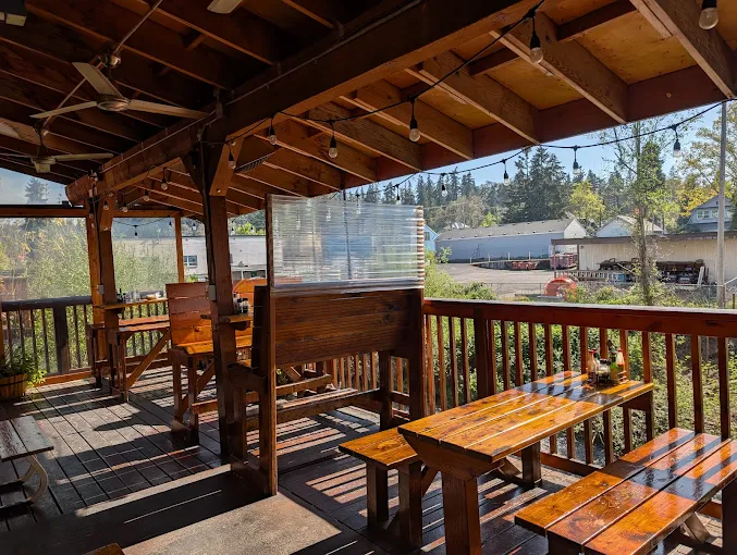 Wooden tables and benches on Mac’s Place covered deck with views across Silver Creek in Silverton, Oregon