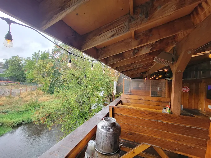 Covered wooden deck with string lights overlooking Silver Creek at Mac’s Place in Silverton, Oregon