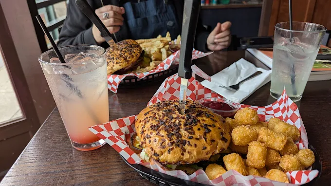Burger and golden tater tots in a basket at Mac’s Place, with drinks and another meal on the table