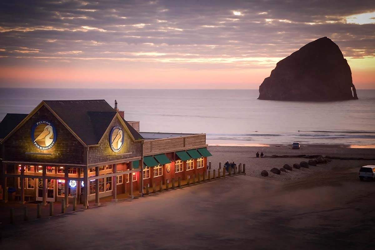 pelican Pelican Brewing in Pacific City, Oregon, beside the beach at sunset, with Haystack Rock rising from the ocean.