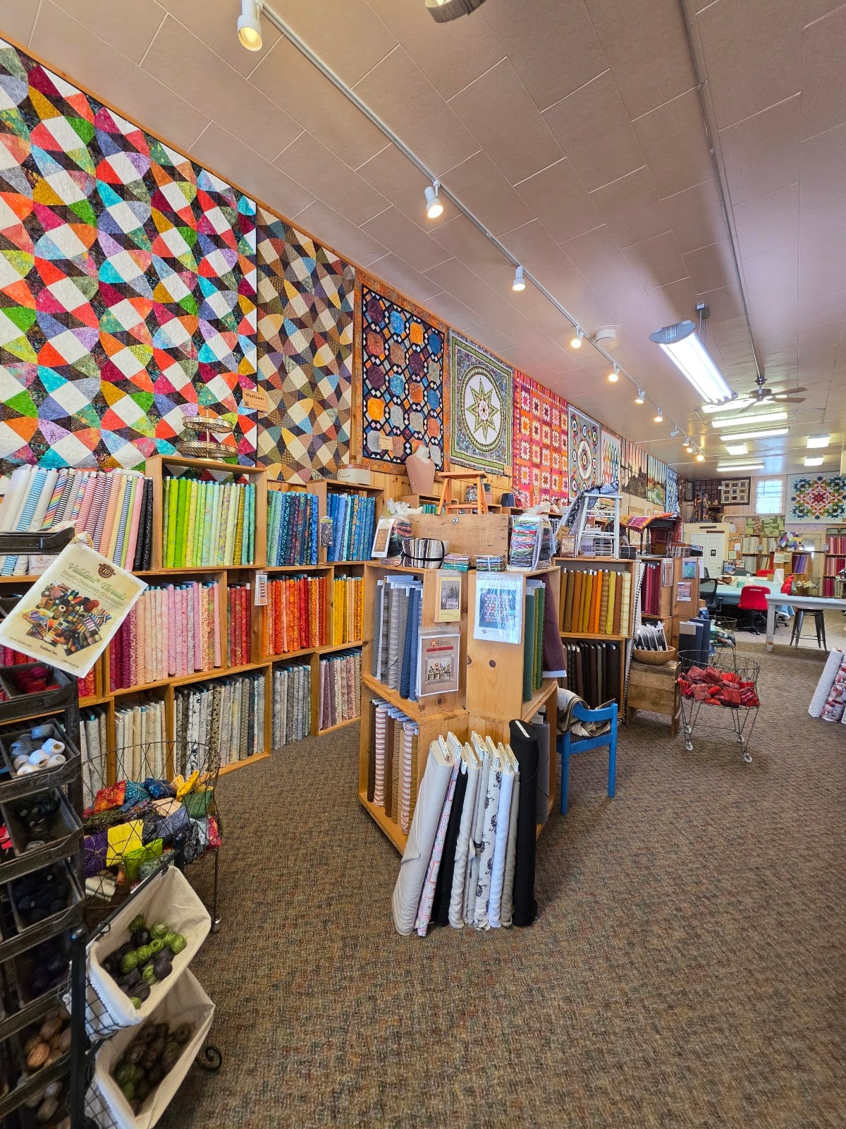 Finished quilts hang above rows of fabric inside Tater Patch Quilts.