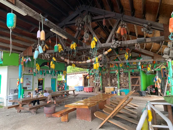 Wooden picnic tables beneath a covered roof decorated with colorful fishing buoys