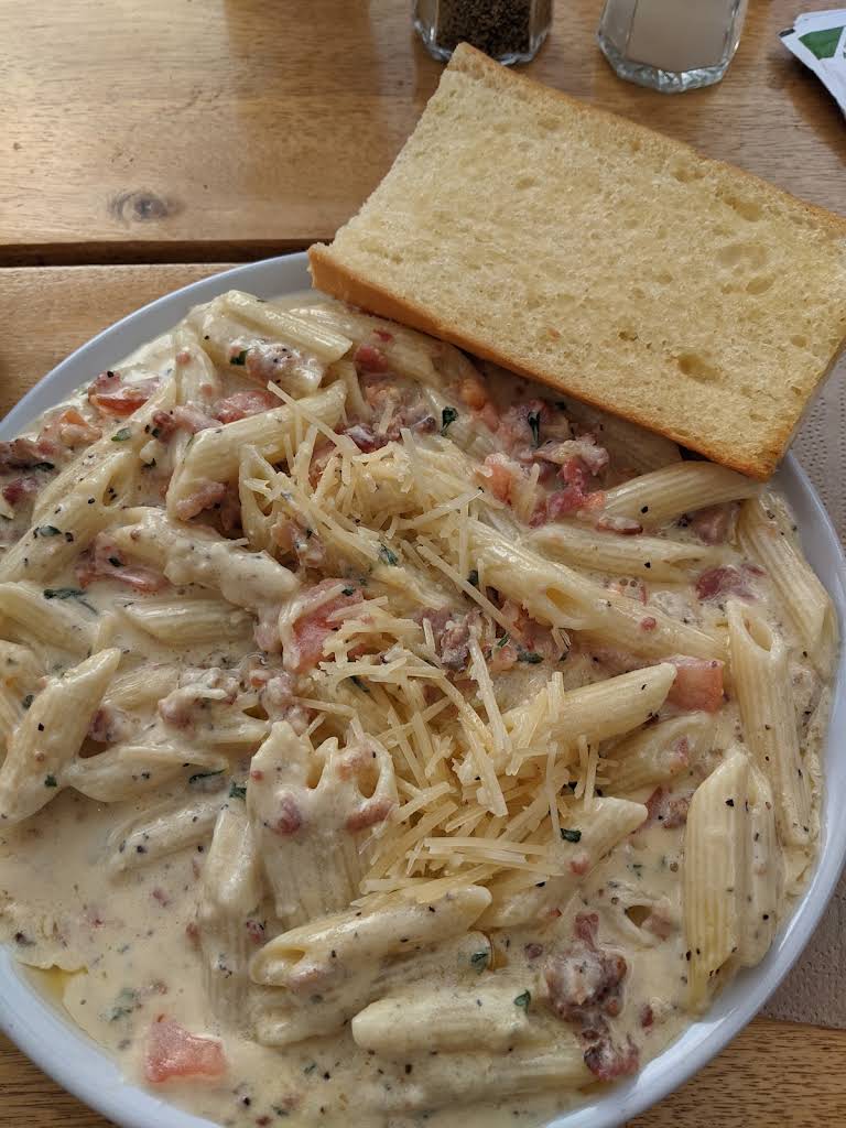 Penne in a creamy sauce topped with shredded cheese and served with bread at Amalfi’s