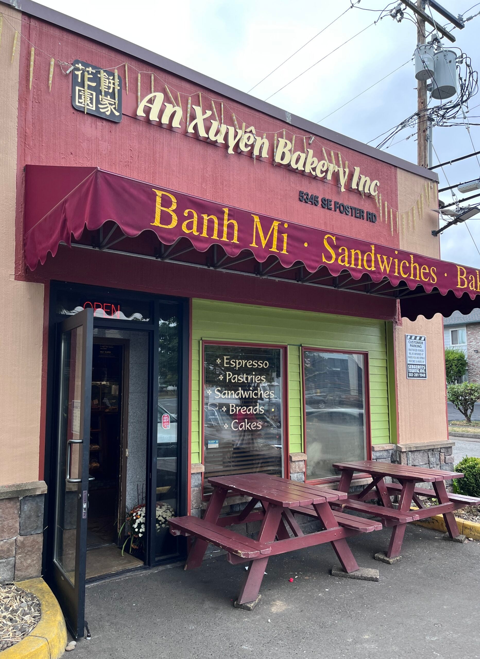 An Xuyên Bakery entrance beneath a red banh mi awning with picnic tables outside, Portland oregon, foster road, vietnamese food, chinese goodies, french baguette, baked fresh daily, bao, bánh mì, cheesecake, cafe, quick snacks, croissants