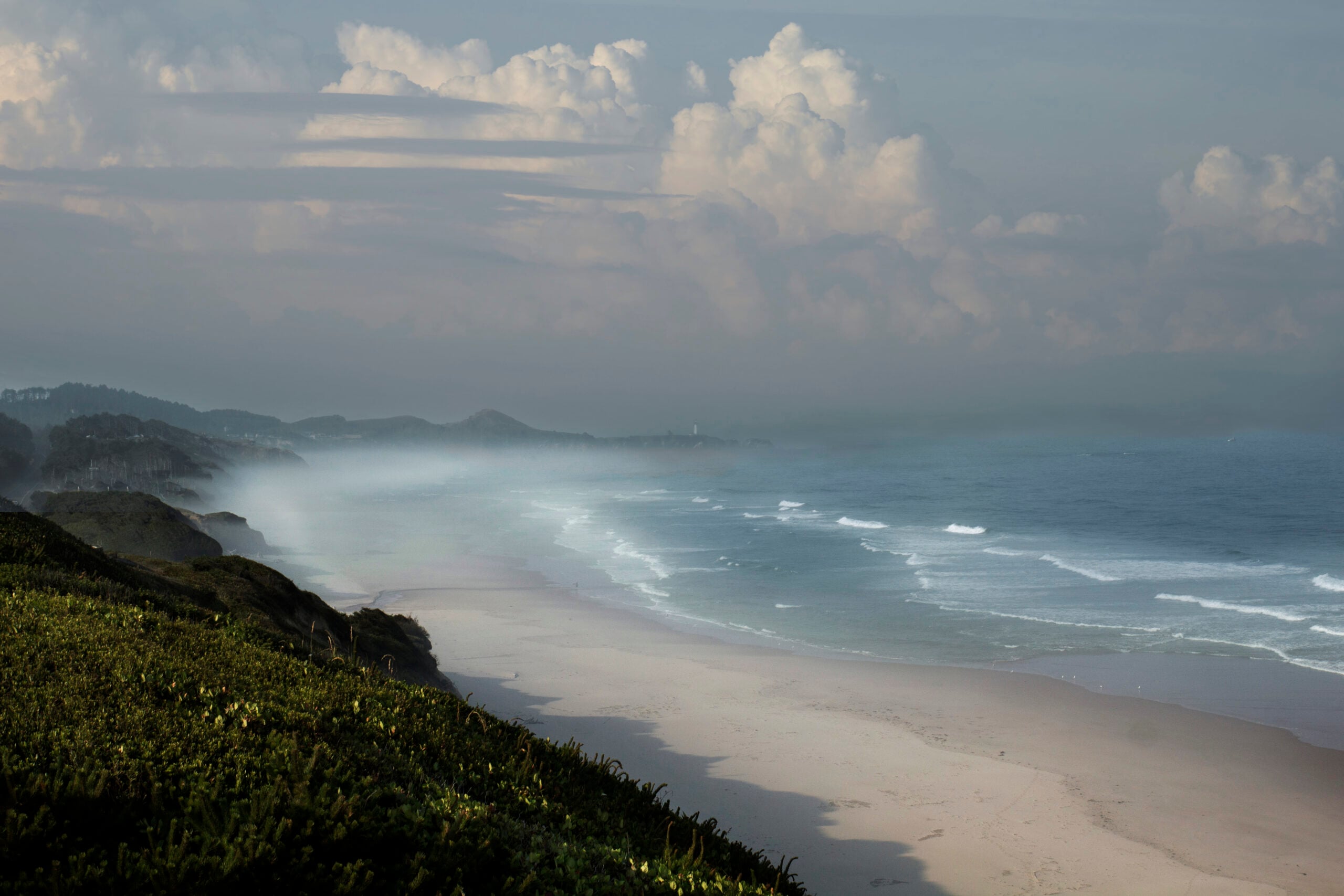 Ocean waves approach a broad sandy beach beneath misty coastal headlands at Beverly Beach.