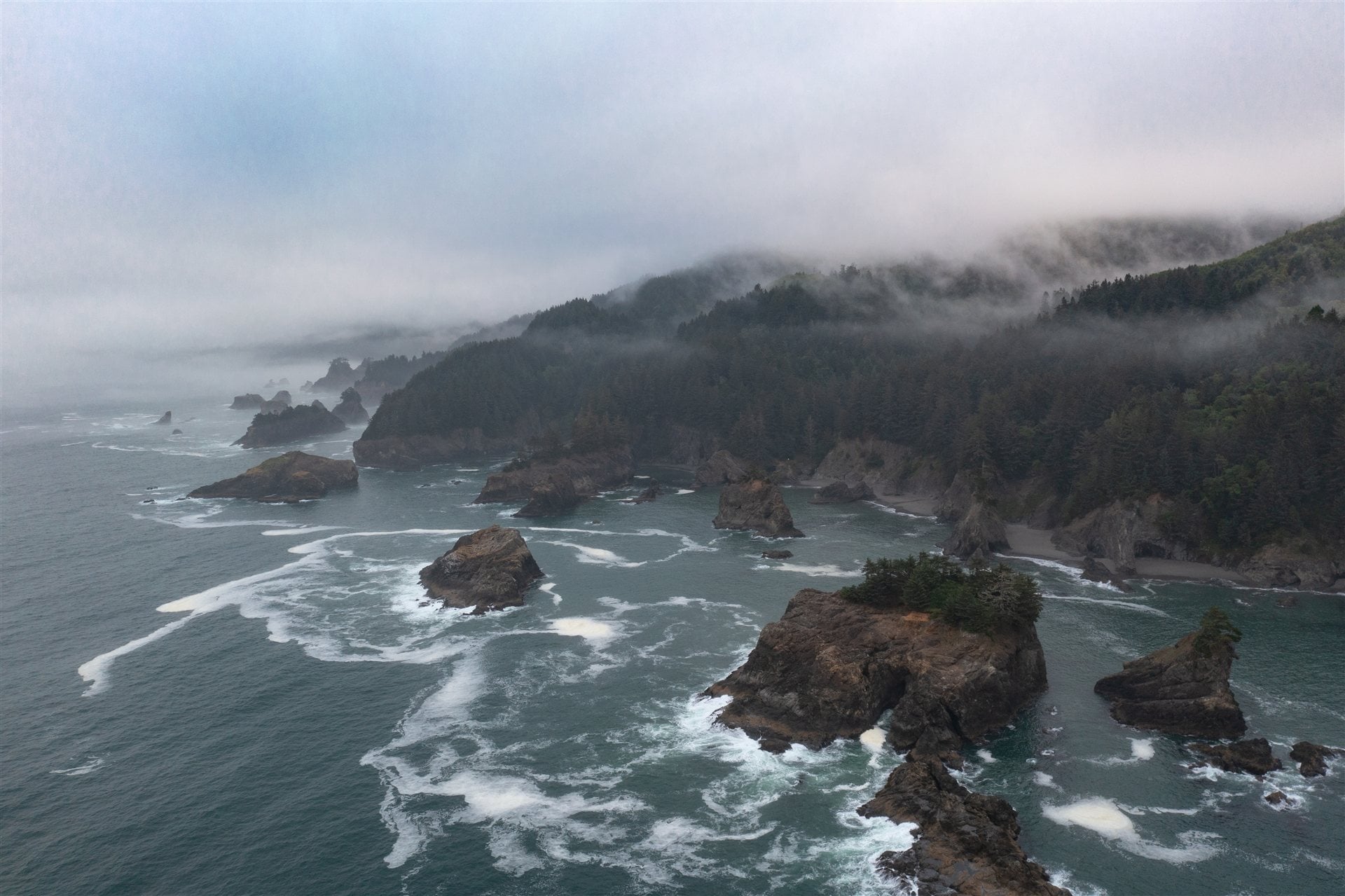 Sea stacks and forested cliffs near Brookings beneath low coastal clouds.