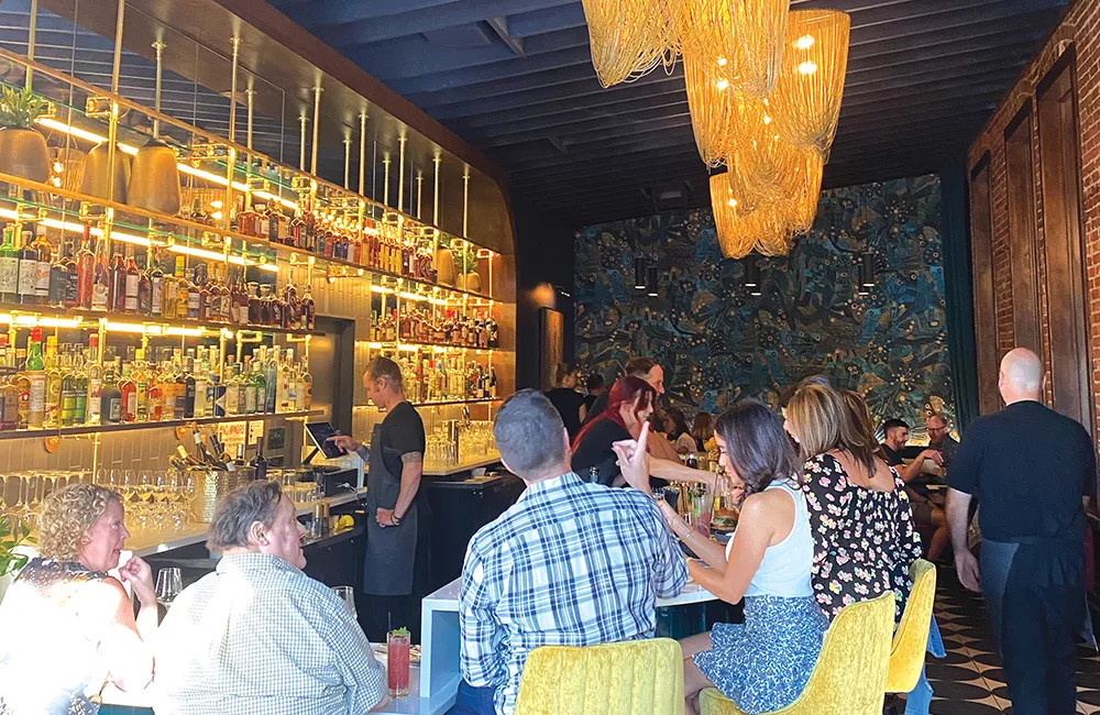 Guests sit at Dear Irene's illuminated bar beneath hanging lights in its colorful Bend dining room