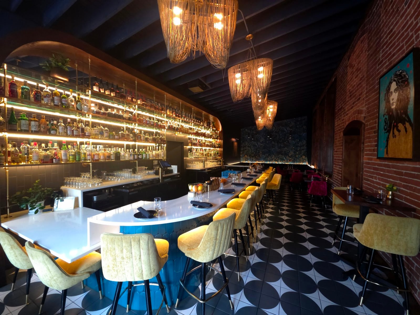 Dear Irene bar and dining room Dear Irene’s illuminated bar, yellow and green stools, hanging gold lights, and patterned floor beside an exposed brick wall