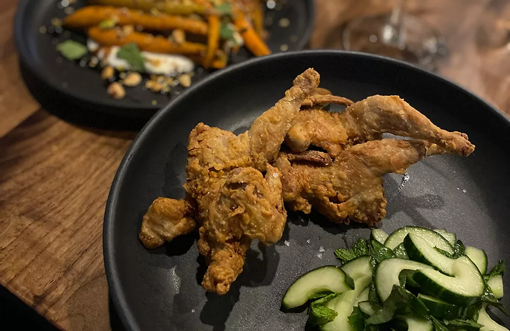 Fried quail and sliced cucumbers on a black plate at Dear Irene