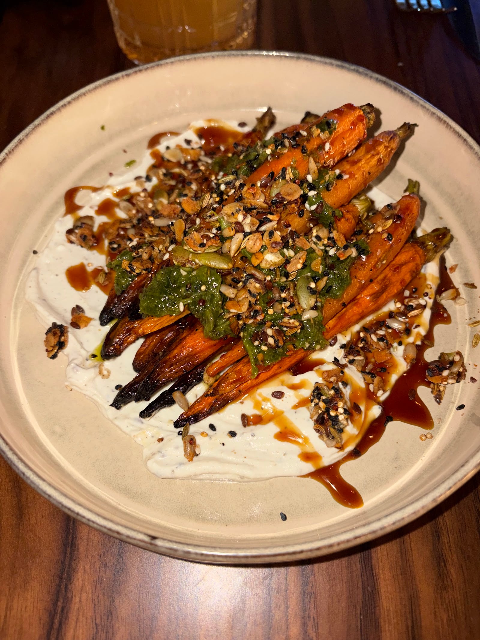 Roasted carrots covered with seeds and green and brown sauces on a white plate