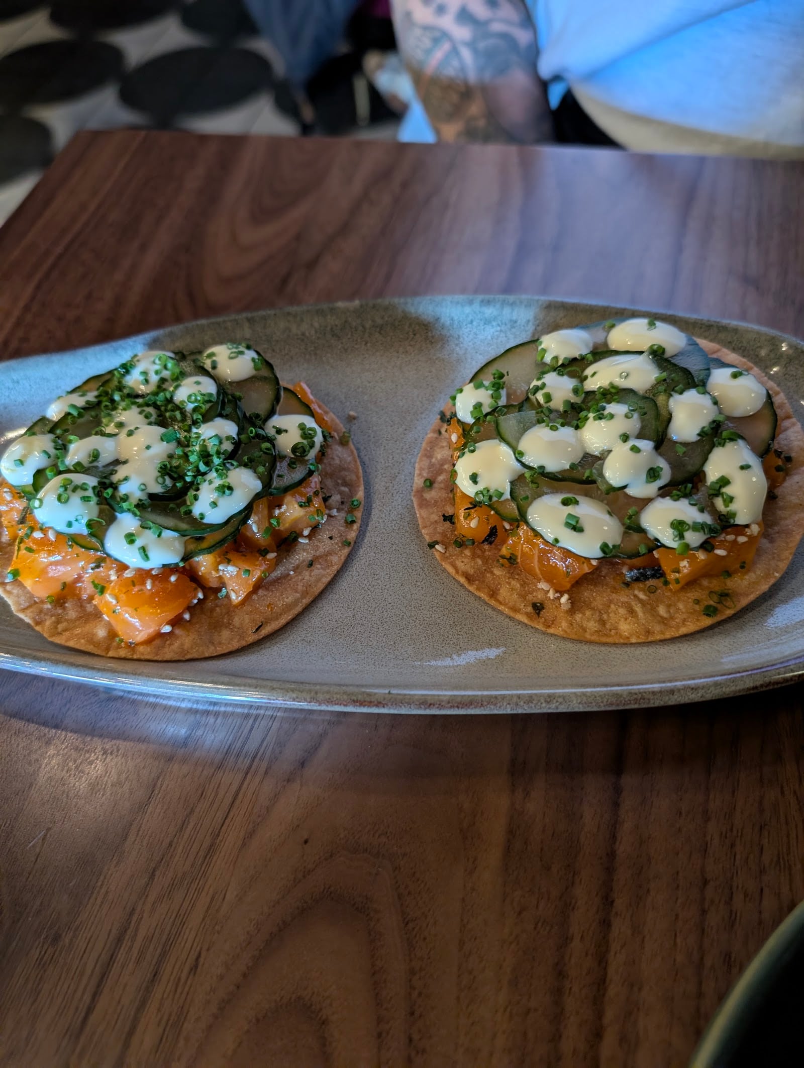 Two tuna tostadas topped with sliced cucumbers, creamy sauce, and chopped chives