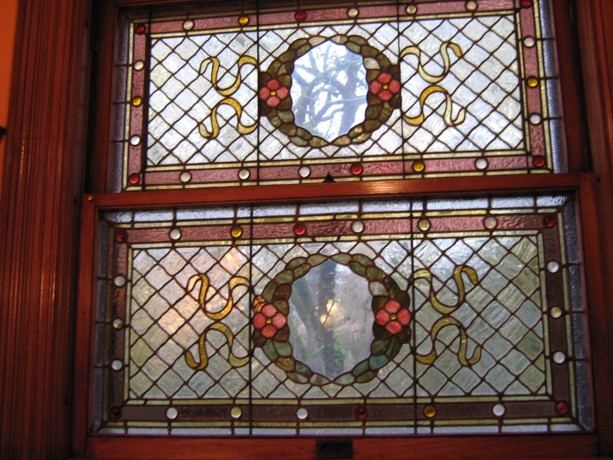 Two decorated stained glass panels with small floral details in a wooden window frame